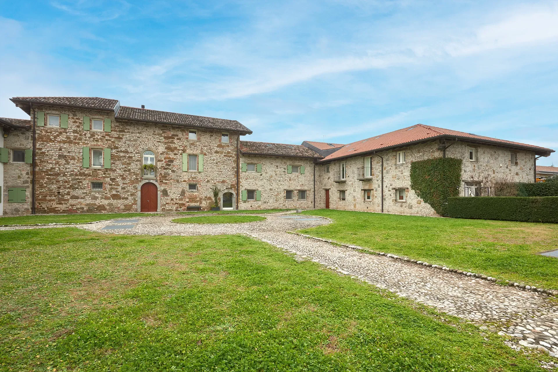 Cortile erboso con edifici in pietra e tetti in coppi, sotto un cielo sereno