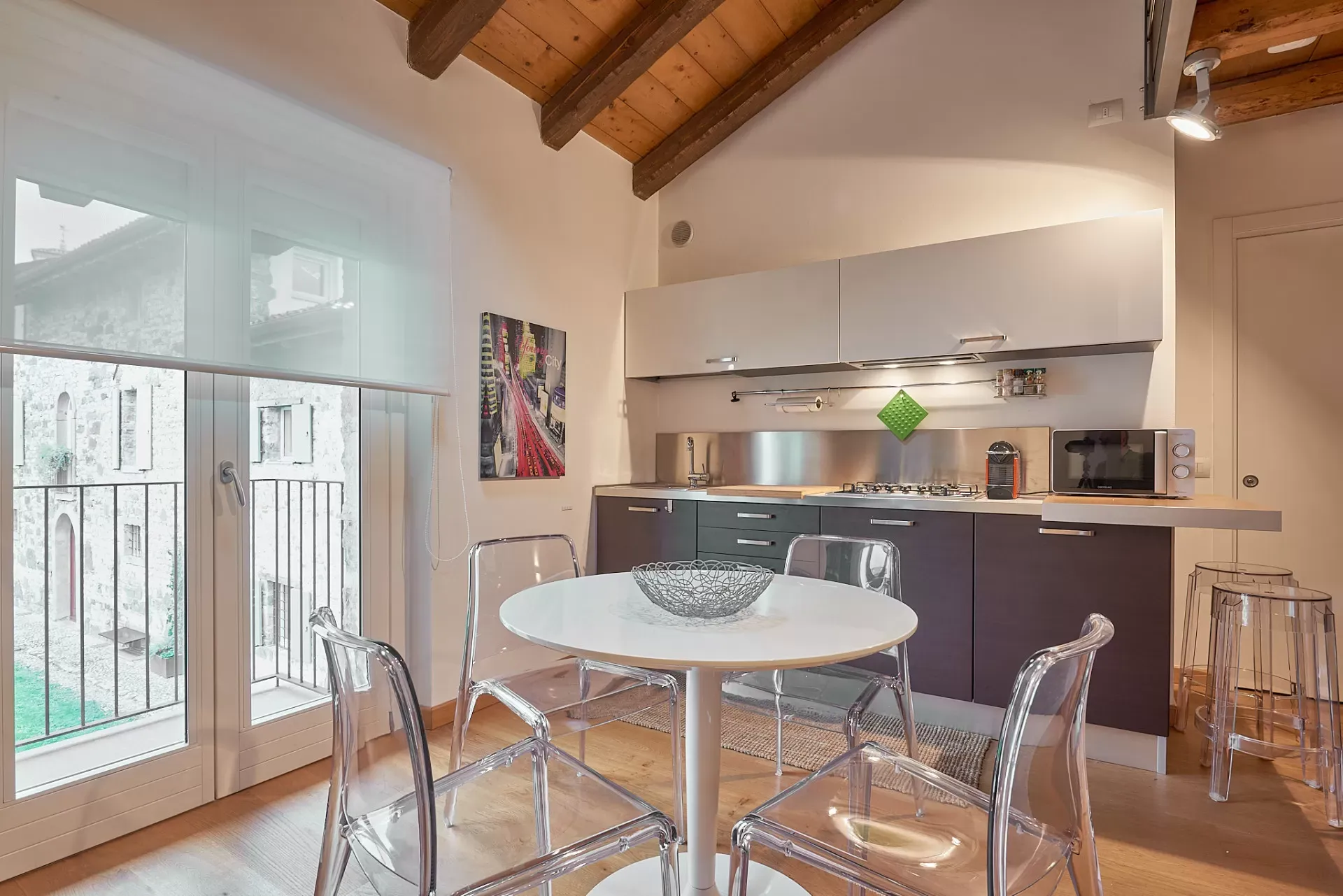 Cucina moderna con tavolo rotondo, sedie trasparenti e grande finestra sul balcone