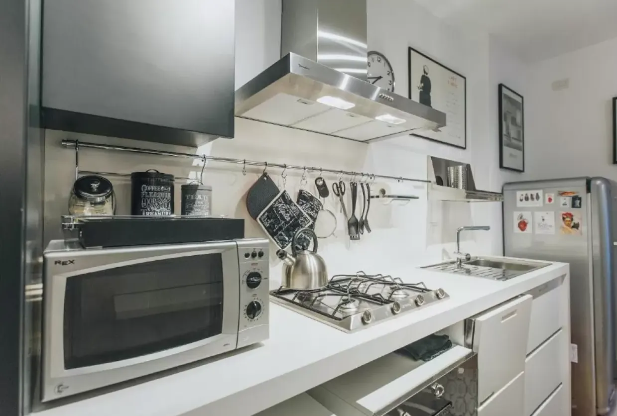 Cucina moderna bianca con piano cottura, microonde, lavello e frigorifero in acciaio inox