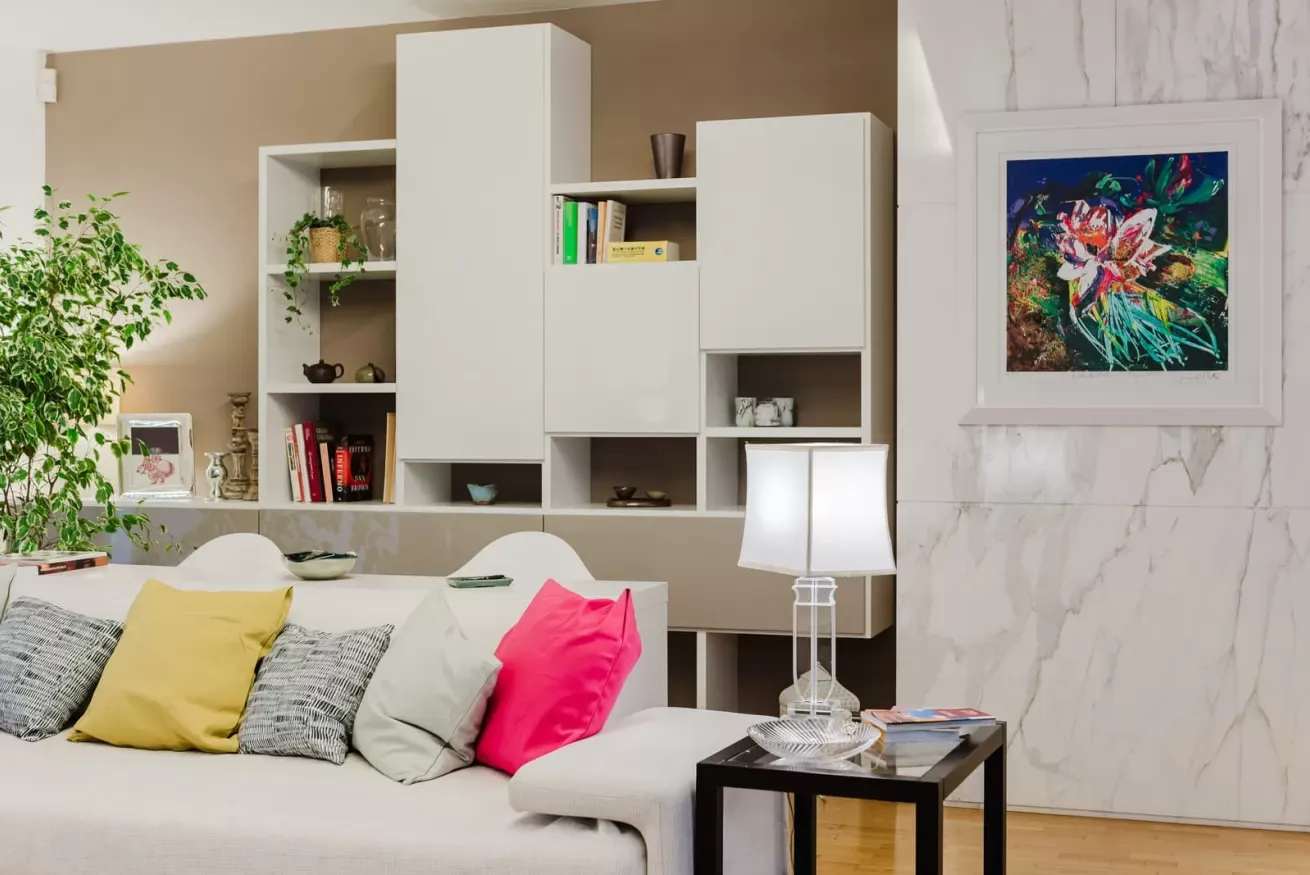 Salotto moderno con divano bianco, cuscini colorati, libreria a parete e quadro floreale incorniciato