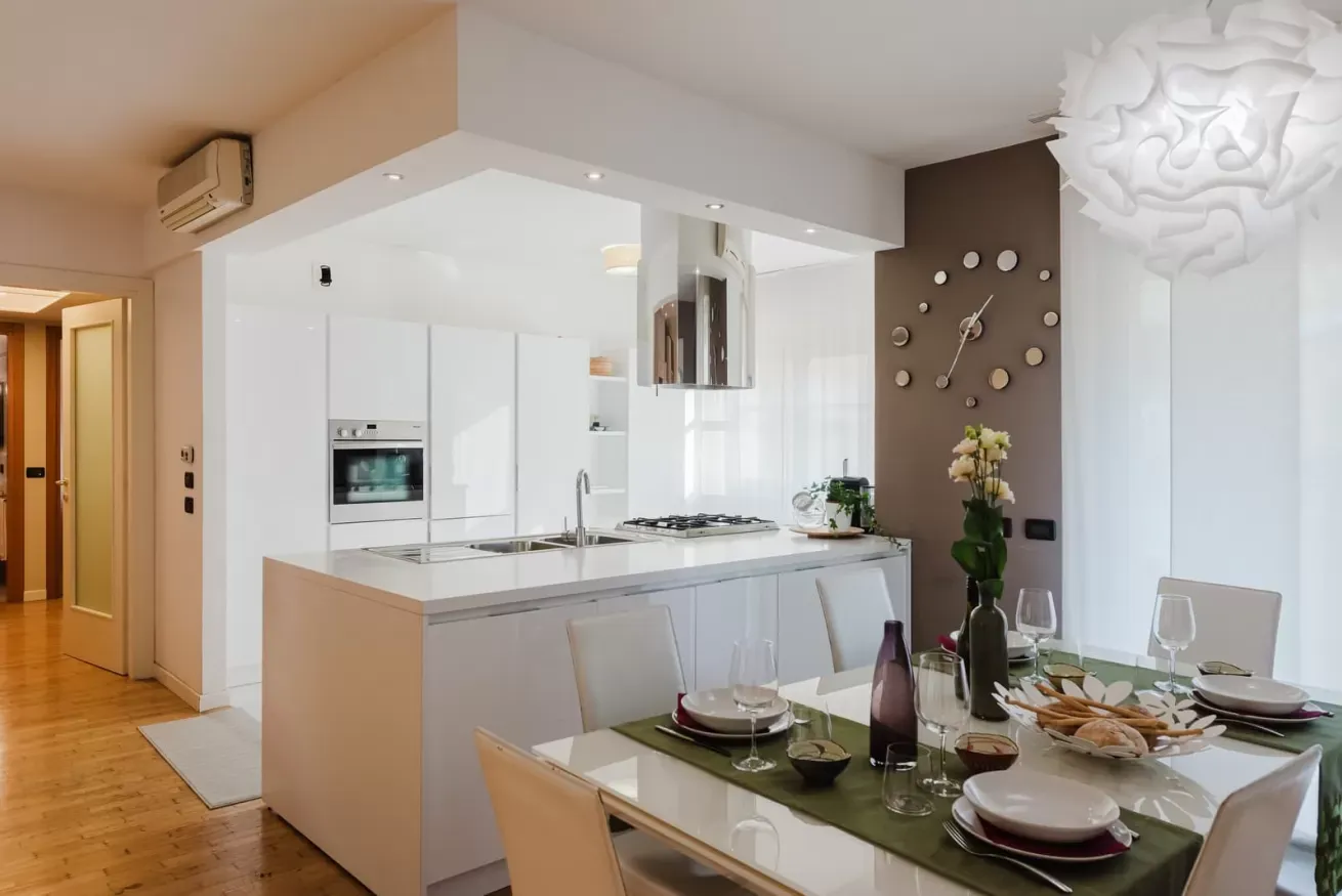 Cucina moderna bianca a vista con tavolo da pranzo apparecchiato e orologio a parete decorativo