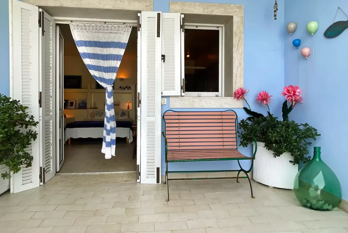 Ingresso di una casa con porte aperte, panca, piante e pareti azzurre decorate con palloncini e fiori