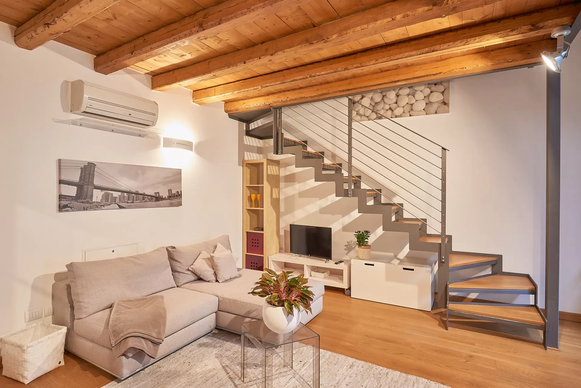 Soggiorno moderno con scala interna in metallo e legno, soffitto con travi a vista e divano angolare