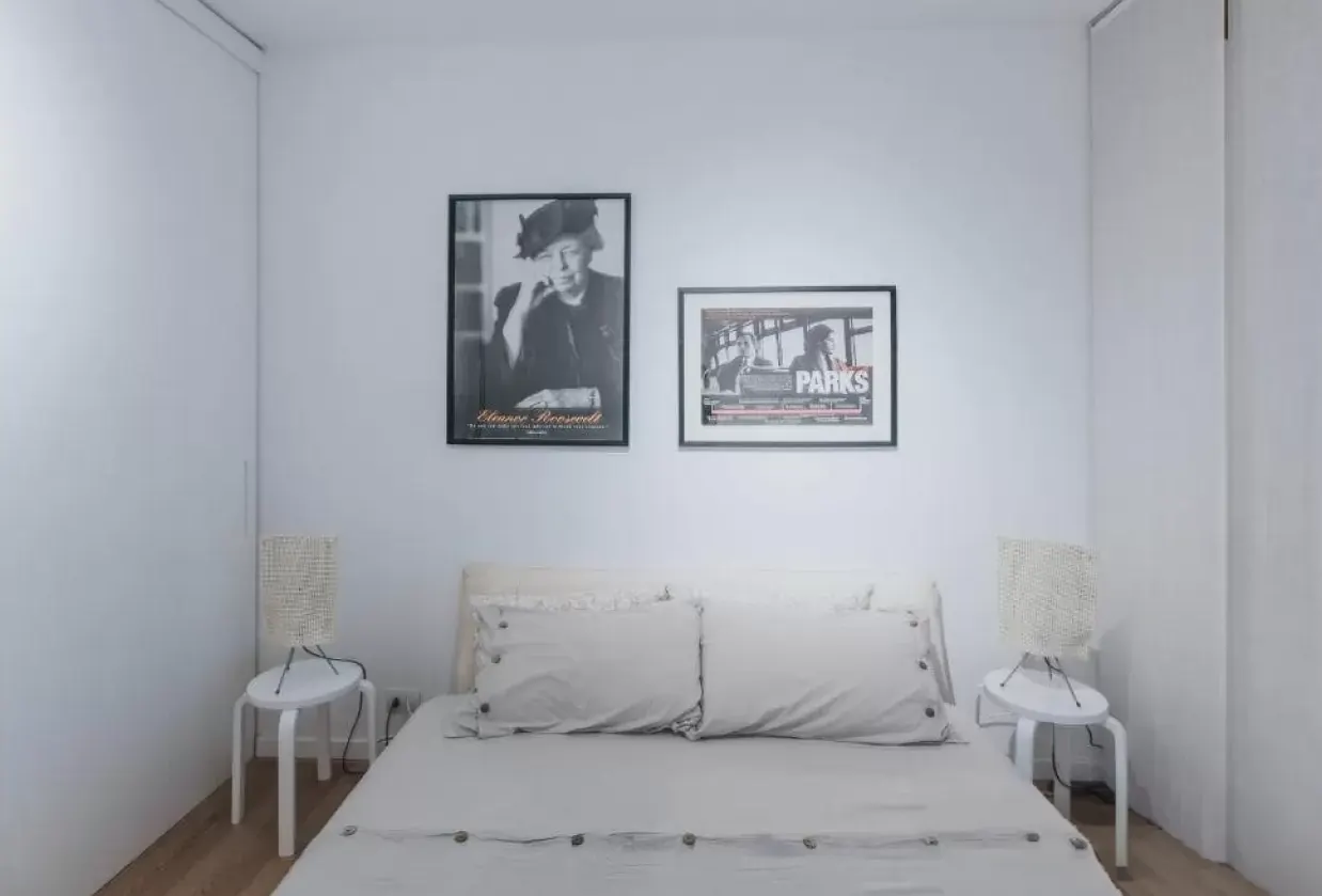 Camera da letto minimalista con letto bianco, due comodini e due quadri in bianco e nero sopra la testata