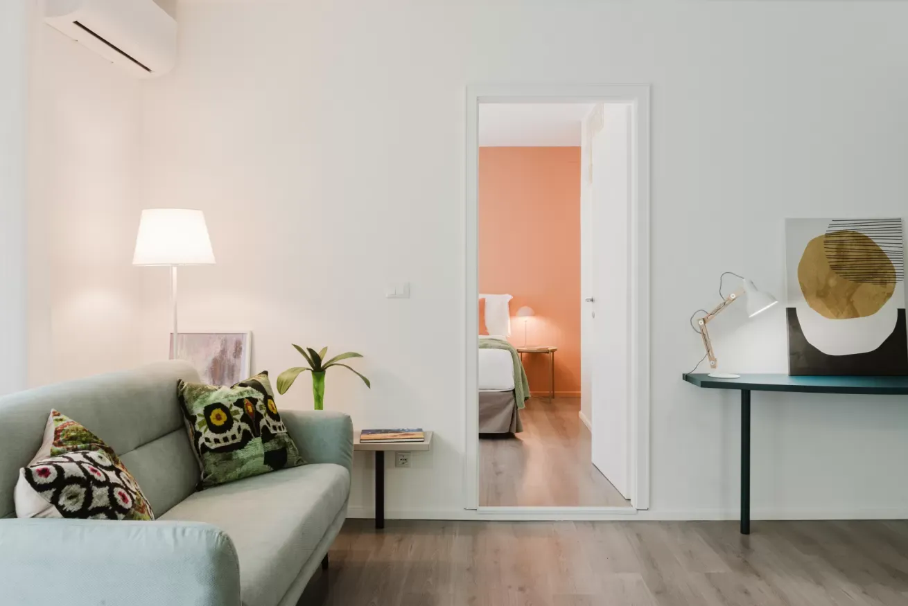 Soggiorno moderno con divano, lampada, tavolino e vista su una camera da letto attraverso la porta aperta