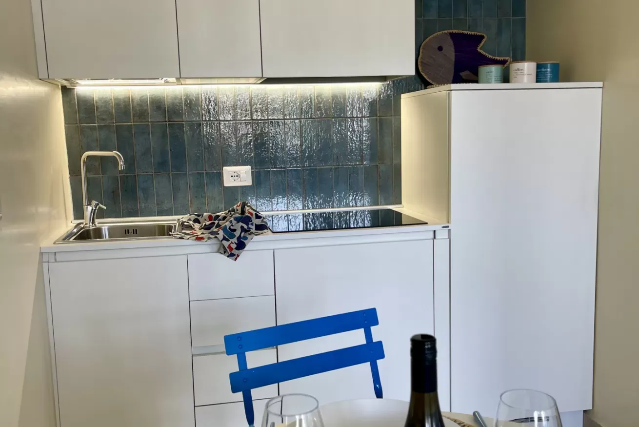 Cucina moderna bianca con piastrelle blu, lavello, piano cottura e frigorifero alto