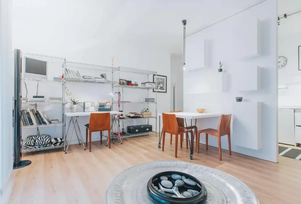 Interno moderno e luminoso con scaffali metallici, tavolo e sedie, e parete bianca divisoria