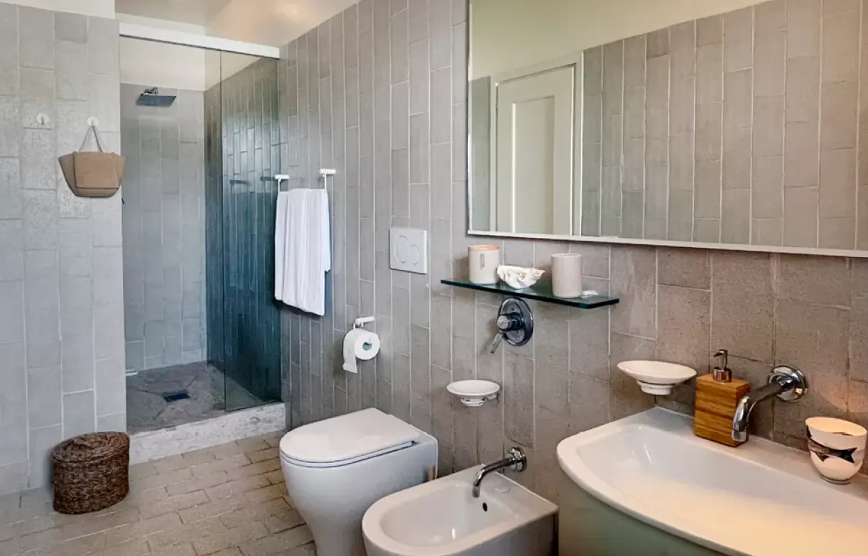 Bagno moderno con doccia in vetro, lavabo, bidet e WC, rivestito in piastrelle grigie