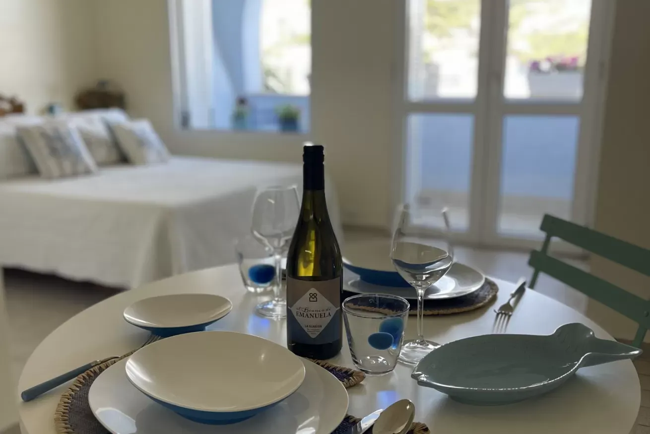 Tavola apparecchiata in una camera da letto, con bottiglia di vino, bicchieri e piatti