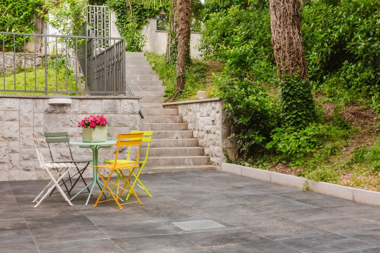 Patio esterno con tavolino e sedie colorate, scale in pietra e vegetazione rigogliosa