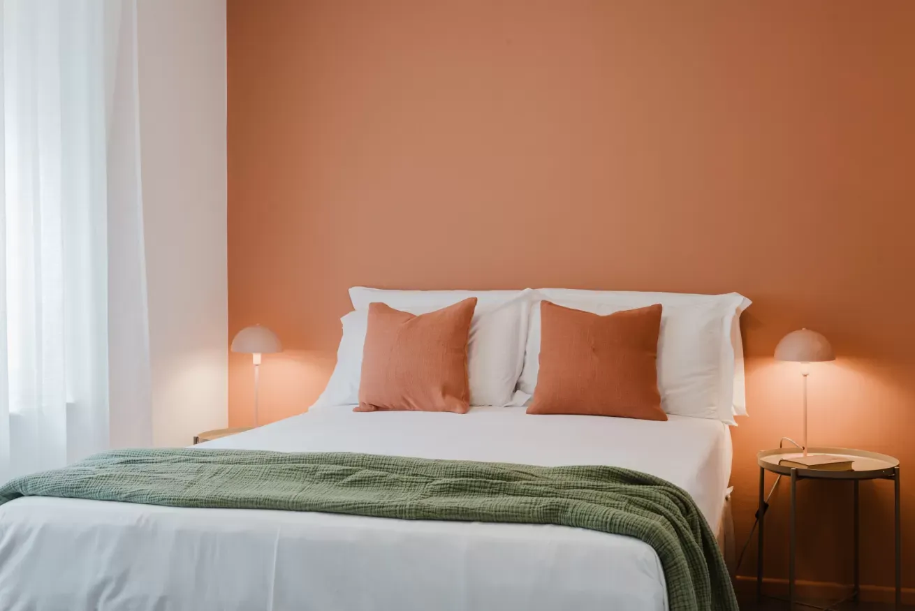 Camera da letto con letto matrimoniale, parete arancione, cuscini color terracotta e coperta verde