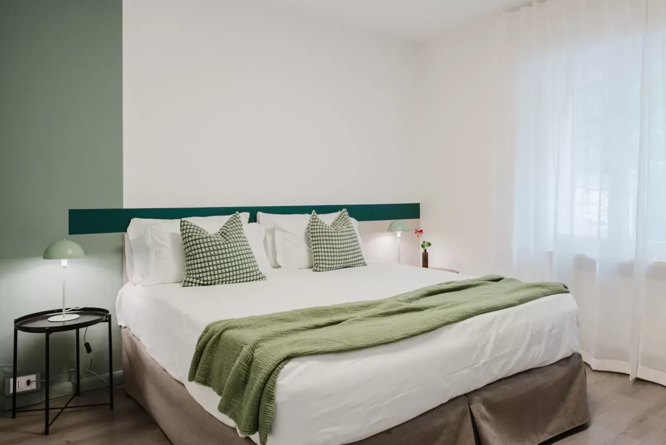 Camera da letto moderna con letto matrimoniale, cuscini verdi e luce naturale dalla finestra
