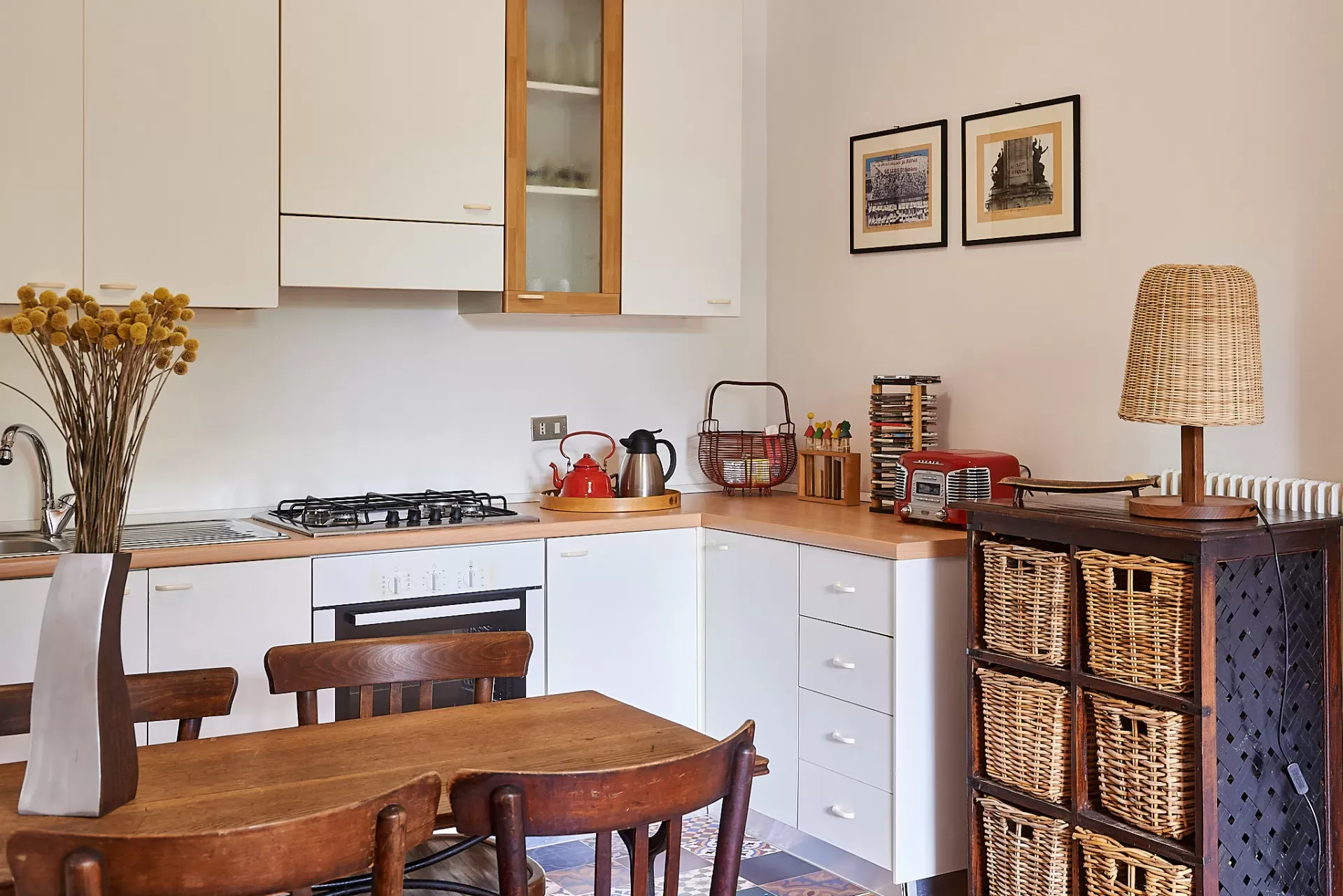 Cucina luminosa con tavolo in legno, mobili bianchi e dettagli in vimini e rosso